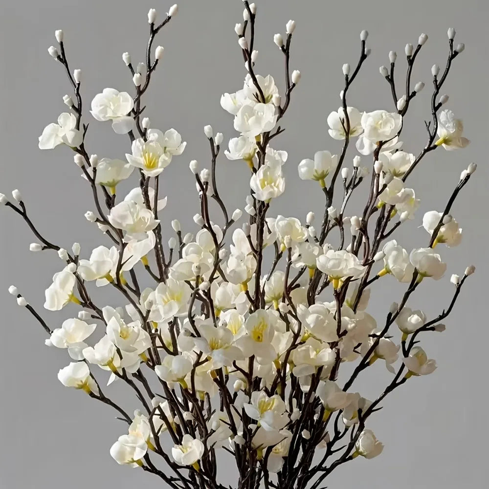 A branch of artificial plum blossoms with white and yellow flowers against a gray background.