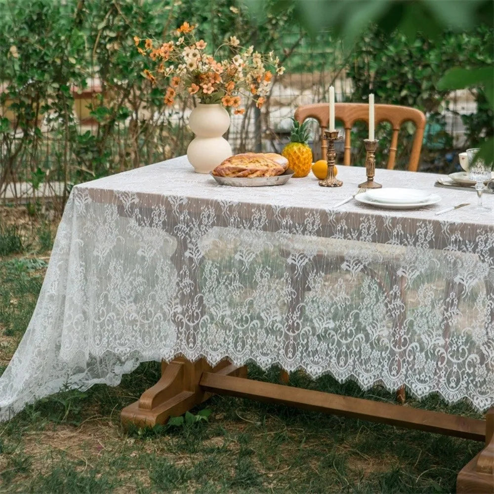 A table set for an outdoor party featuring a lace retro tablecloth, a loaf of bread, and candles.