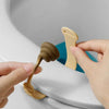 A hand is lifting a beige portable toilet lid lifter from the rim of a white toilet bowl.