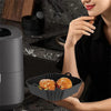 A woman is preparing food in a black reusable silicone air fryer liner on a stovetop.