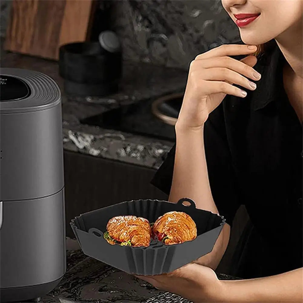 A woman is preparing food in a black reusable silicone air fryer liner on a stovetop.