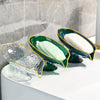 A set of oval green and gold plastic soap dishes with white bars are displayed on a white surface.