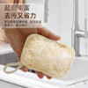 A hand holds a natural beige loofah exfoliating body sponge with a hanging rope over a kitchen sink.