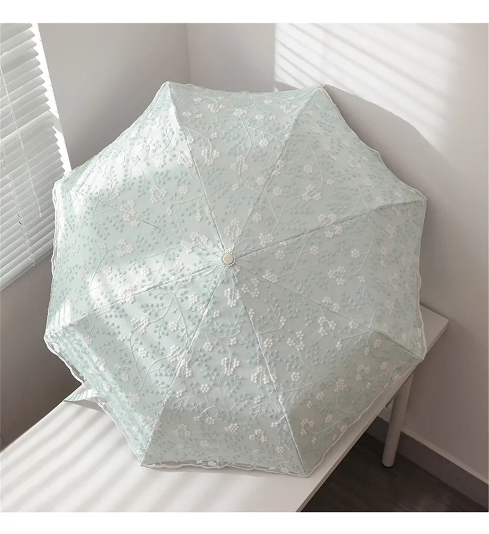 A light blue embroidered sun umbrella is shown open on a white surface.