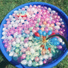 A blue bowl filled with numerous pink, purple, and clear water balloons on green grass.