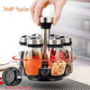 A hand is rotating a glass spice jar rack with stainless steel lids on a rotatable base.