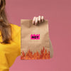 A hand is holding a brown paper bag with a pink hot sticker on it against a pink background.