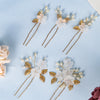 A set of pearl and gold floral bridal hair clips displayed on a light blue background.