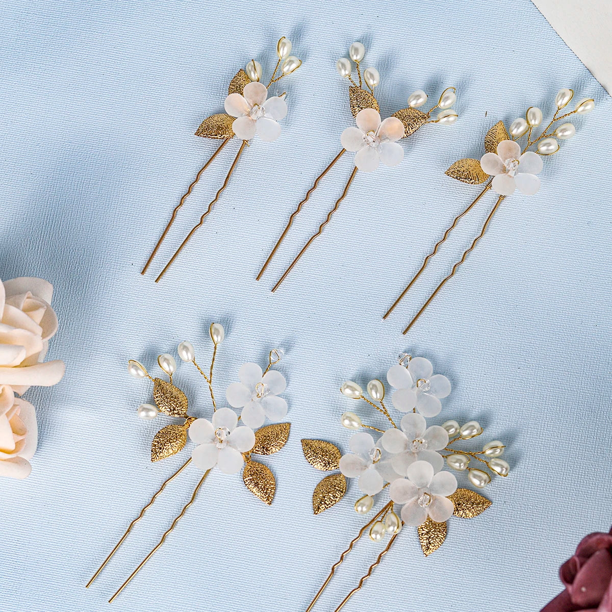 A set of pearl and gold floral bridal hair clips displayed on a light blue background.