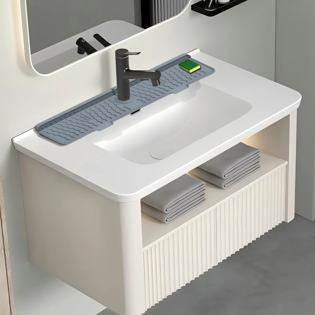 A white kitchen sink features a silicone splash guard mat with a faucet and a green soap dispenser.