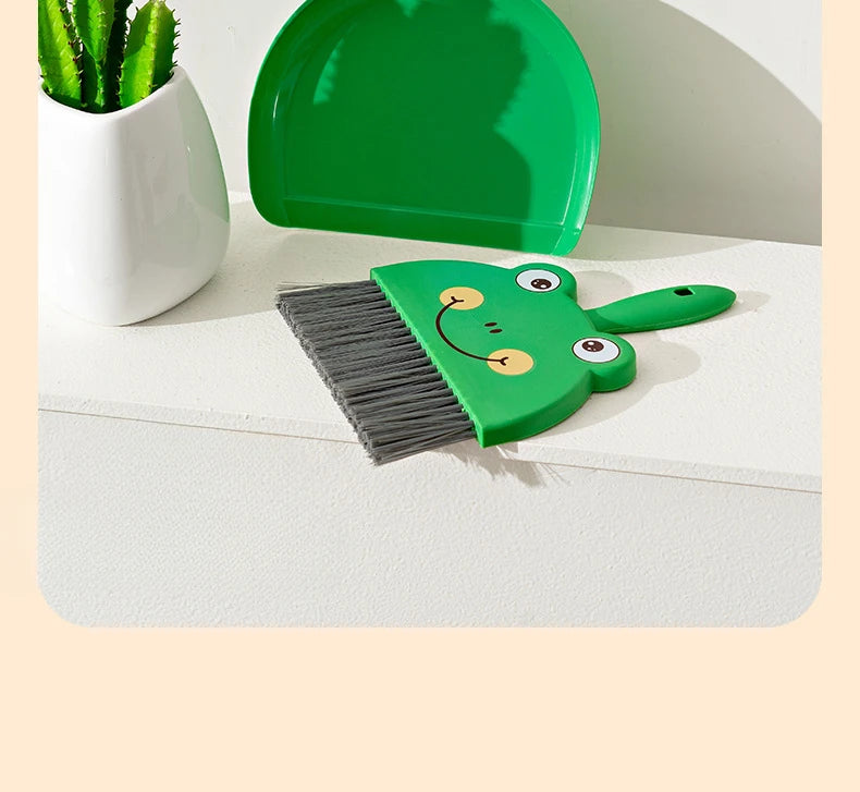 A set of green cartoon animal broom and dustpan with a white potted plant in the background.
