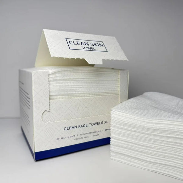 A box of clean face towels and a stack of white facial cleansing wipes are displayed on a white surface.