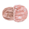 A pink reusable satin lined shower cap with a white leaf pattern.