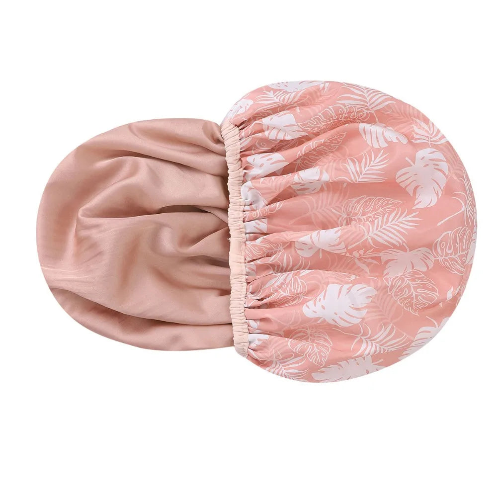 A pink reusable satin lined shower cap with a white leaf pattern.