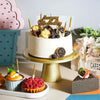 Mehrstöckige Torte mit goldenen Kerzen und Früchten auf goldenem Ständer neben kleinen Desserts