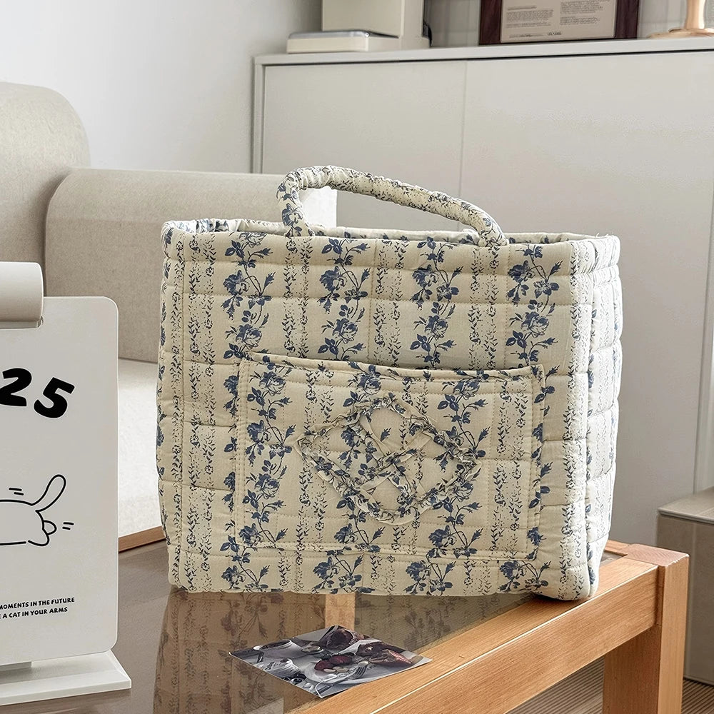 A beige floral storage basket with a handle featuring blue and gray botanical patterns sits on a wooden surface.