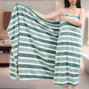 A woman holds a striped teal and white bath towel draped over her shoulder.