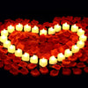 A heart shape formed by glowing white LED tea lights surrounded by red artificial rose petals.