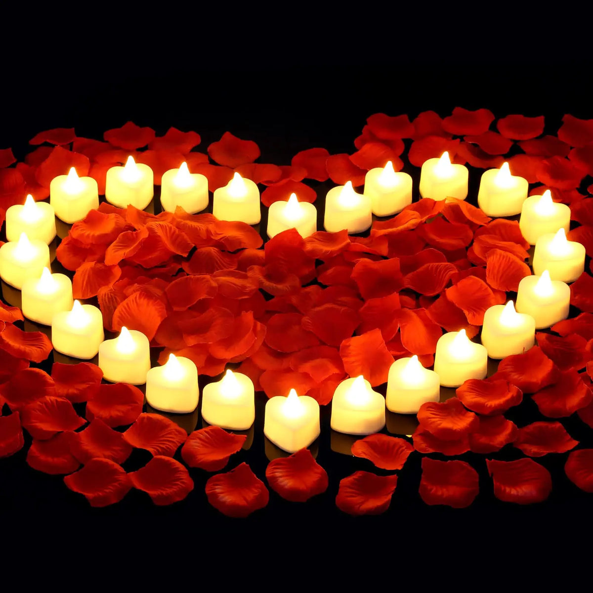 A heart shape formed by glowing white LED tea lights surrounded by red artificial rose petals.