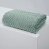 A folded teal coral velvet bath towel with a geometric quilted pattern resting on a white surface.