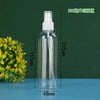 A clear glass refillable portable spray bottle with a white cap and a long white nozzle, shown next to a green plant.