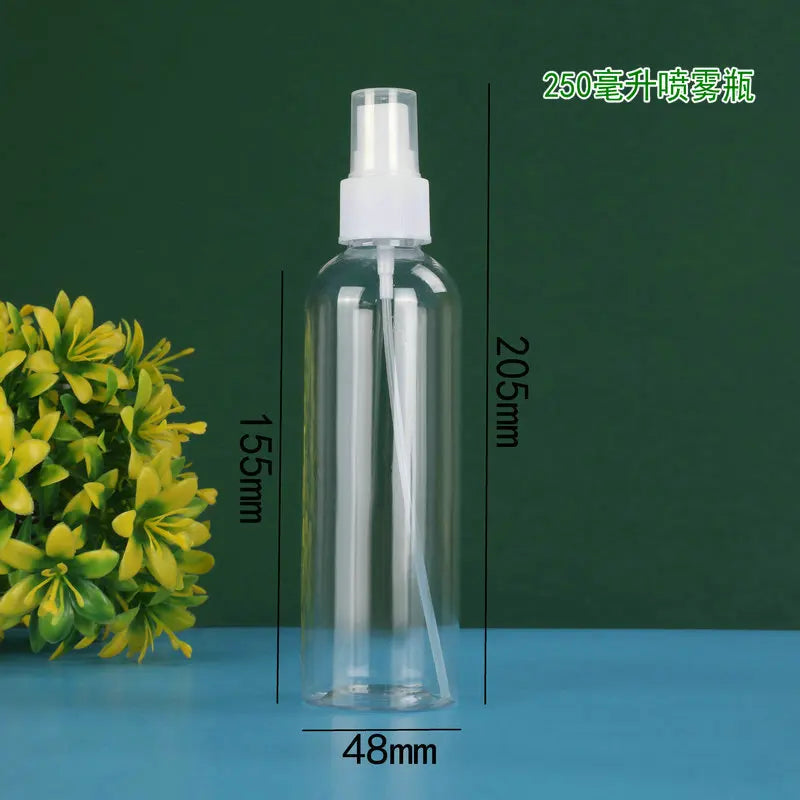 A clear glass refillable portable spray bottle with a white cap and a long white nozzle, shown next to a green plant.