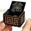 An antique wooden hand crank music box with a lid displaying the word QUEEN and an ornate design.