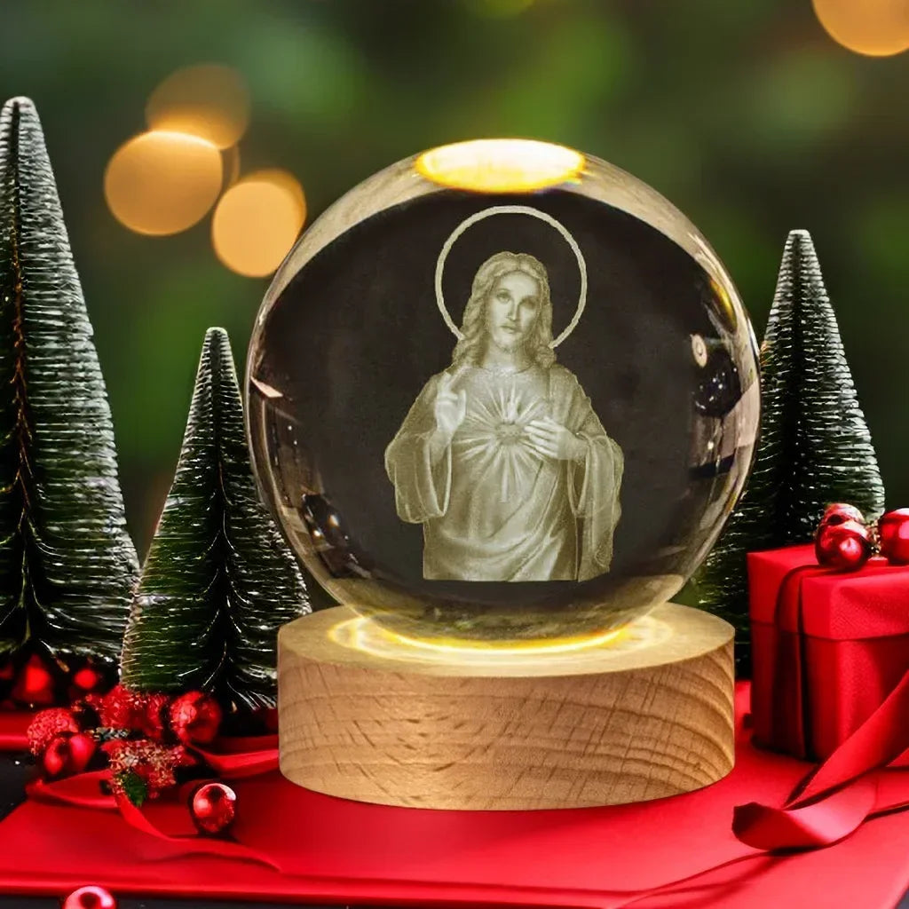 A glass crystal ball with a depiction of Jesus, set on a wooden base, surrounded by green pine trees and red ribbon.