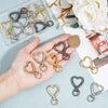 A hand holds a collection of heart-shaped spring hook keychains in various gold and silver tones on a light blue surface.