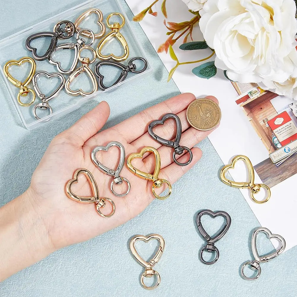 A hand holds a collection of heart-shaped spring hook keychains in various gold and silver tones on a light blue surface.