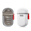 A clear plastic leakproof portable soap dish with a gray lid and red handle, shown next to its white, ribbed body.
