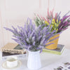 A bouquet of artificial lavender flowers in a white vase sits on a white surface.