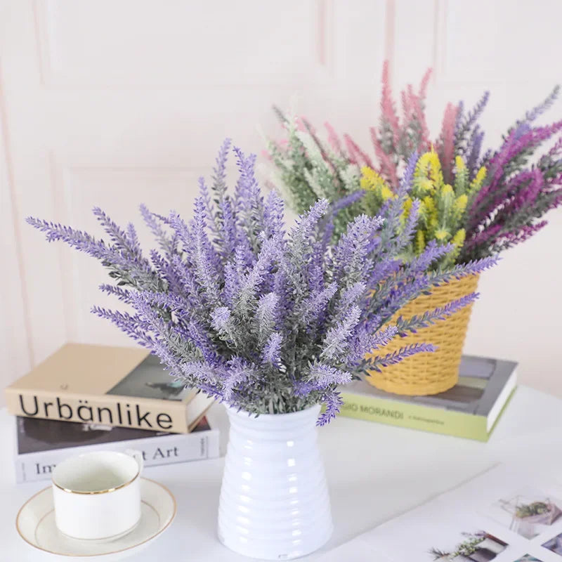 A bouquet of artificial lavender flowers in a white vase sits on a white surface.