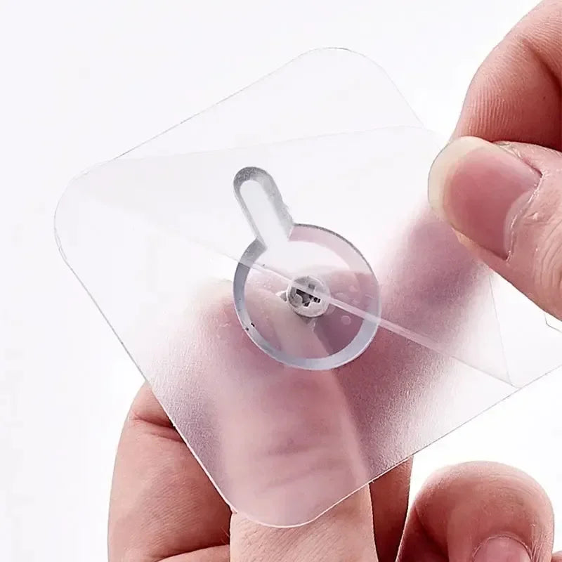A hand holds a transparent self-adhesive wall hook for frames and photos, showing the adhesive backing.