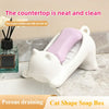 A white cat-shaped soap box with a purple soap dispenser sits on a marble countertop.
