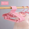 Pink plastic hangers with bow designs for kids, shown hanging on a wooden rod.