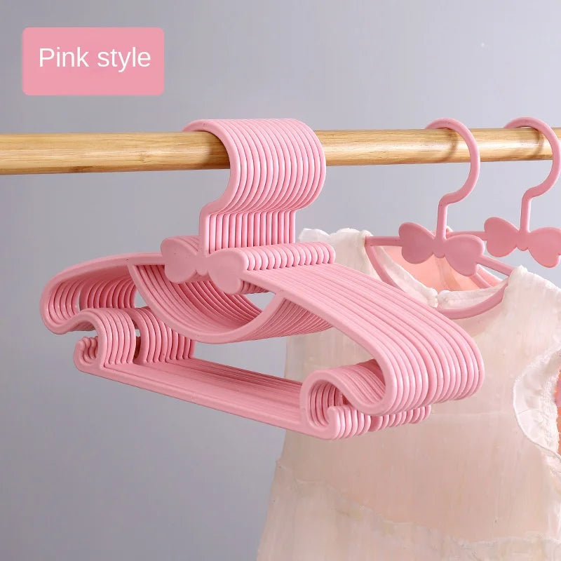 Pink plastic hangers with bow designs for kids, shown hanging on a wooden rod.