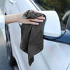 A hand is holding a dark gray microfiber cleaning cloth against the white exterior of a car.