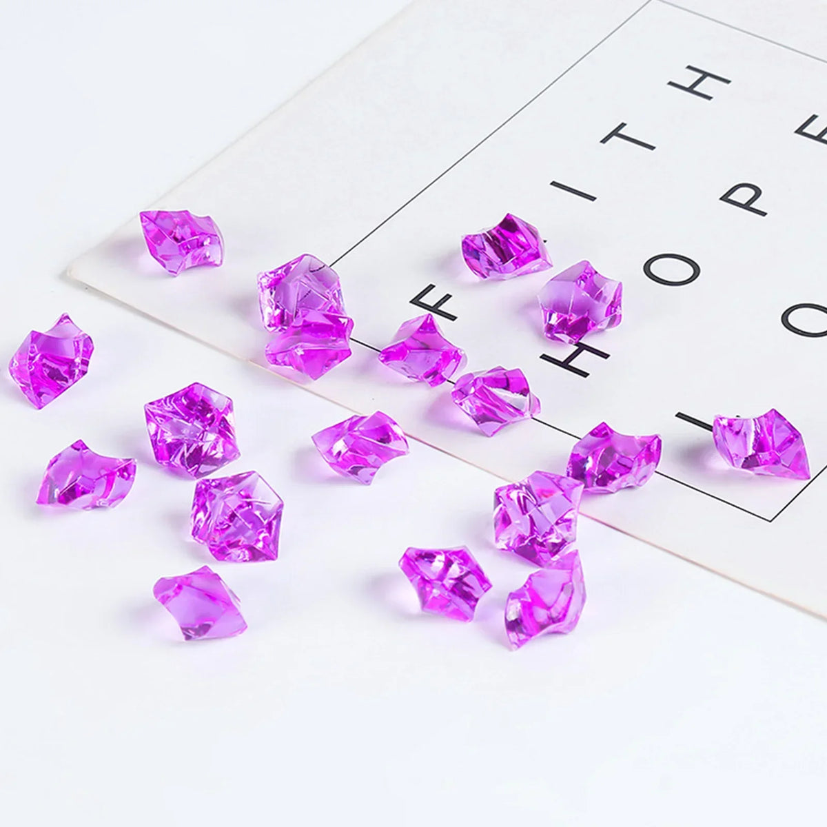 A collection of crushed purple and pink crystal ice stones scattered on a white surface next to the word hope