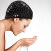 A woman wearing a black adjustable mesh wig cap, looking down and touching her face.