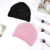 A black mesh wig cap is displayed next to a pink floral mesh wig cap on a white marble surface.