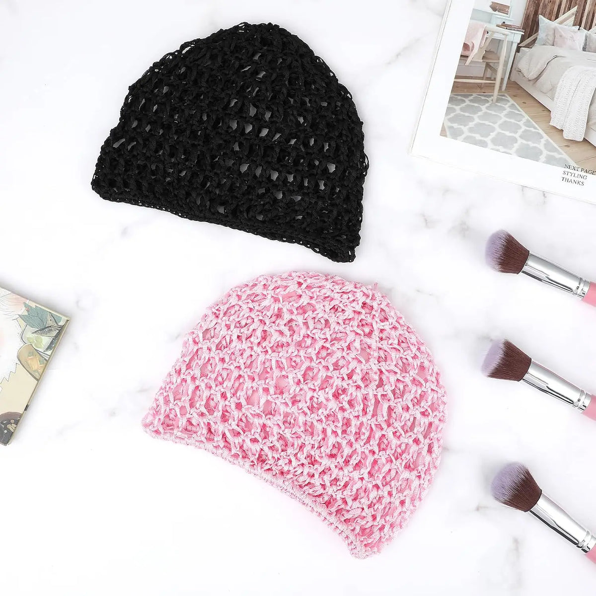 A black mesh wig cap is displayed next to a pink floral mesh wig cap on a white marble surface.