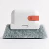 A white window and gap cleaning brush with an orange cleaning head resting on a gray felt surface.