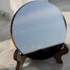 A round black obsidian scrying mirror decor resting on a wooden stand.