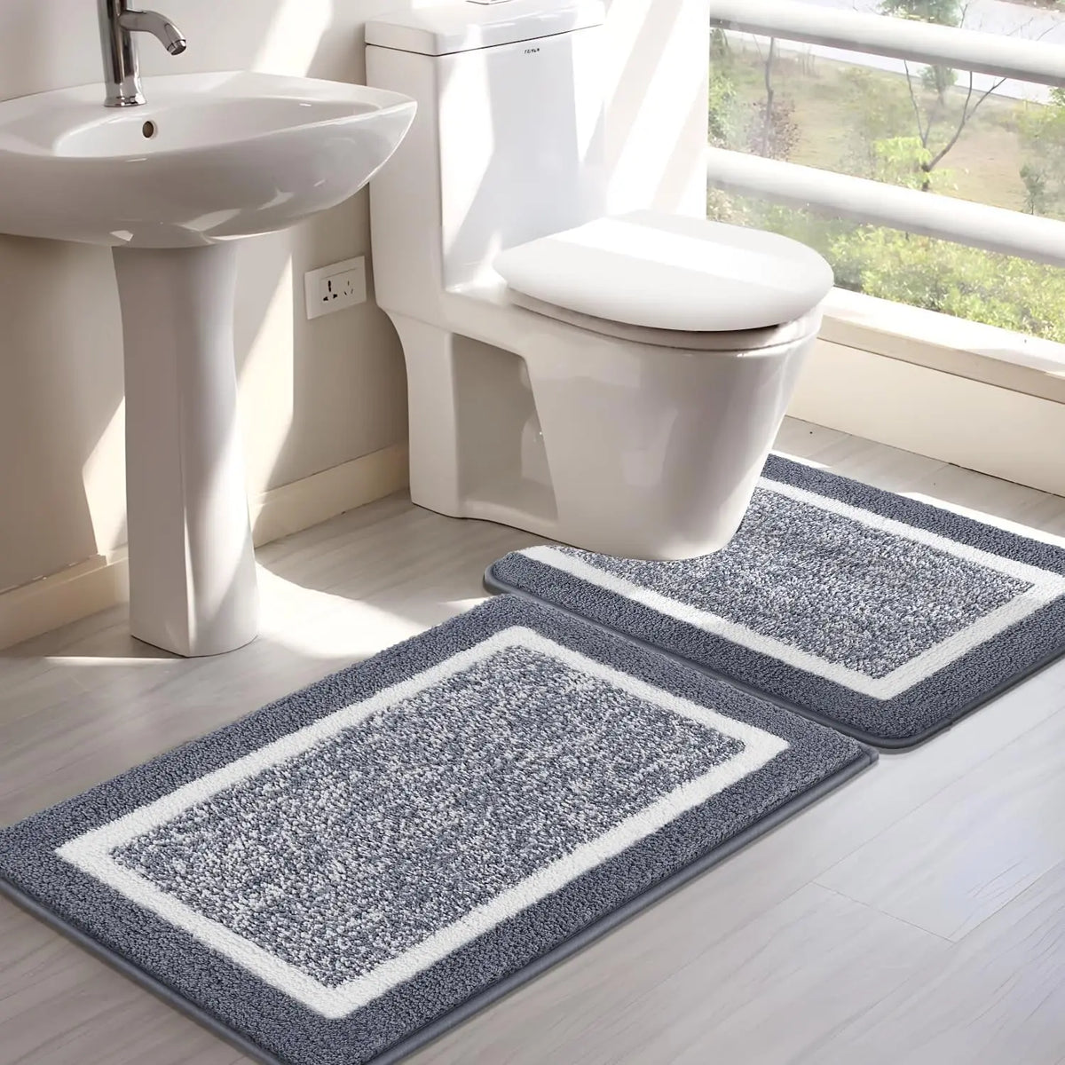 A white toilet and sink area with two gray microfiber non-slip bath mats on the floor.