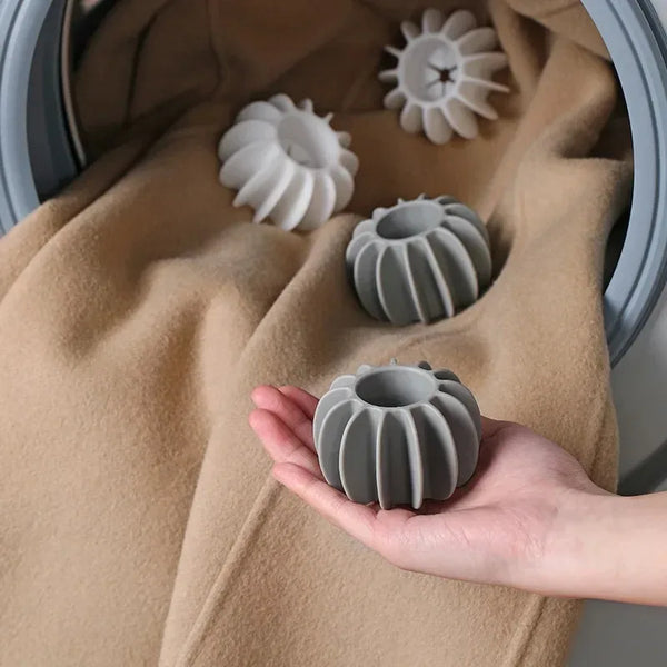 A hand holds a gray reusable laundry ball for pet hair and lint removal against a tan fabric background.