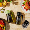 A green glass olive oil dispenser and a dark glass extra virgin olive oil bottle are displayed on a light surface.