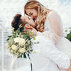 A close-up photo of a couple embracing, with a bouquet of white roses and baby's breath flowers.