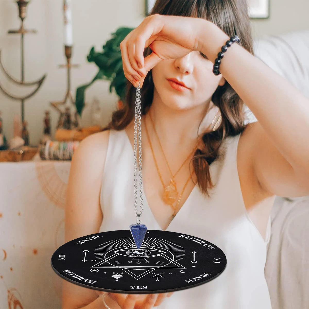 A woman holds a black divination circle with a silver pendant and a crystal necklace against a white background.