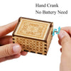 A hand is holding a vintage engraved wooden music box with a hand crank for operation.